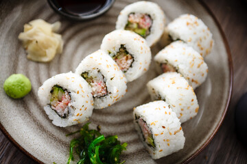 Sushi maki rolls California with crab, cucumber and avocado on a plate with chopsticks, soy sauce, wasabi and ginger. Japanese traditional seafood served for lunch in modern gourmet restaurant