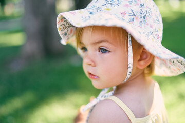 Little girl in a panama hat stands on a green lawn. Portrait