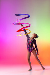 Young professional female rhythmic gymnast exercising with bright ribbon isolated on multicolored...