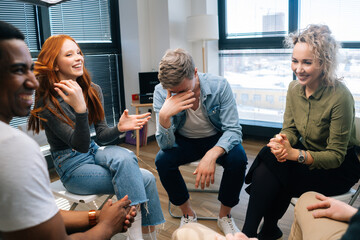 Group of cheerful young activity diverse multiethnic colleagues laughing during brainstorming near window. Happy creative coworkers working together in teamwork discuss project plan in office.