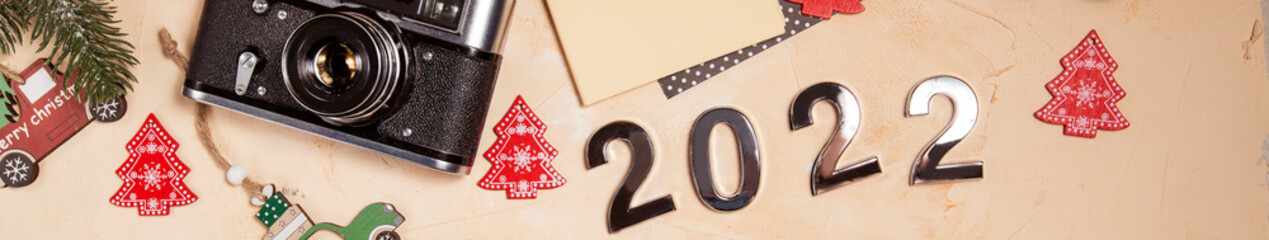 Christmas background with toys, Christmas tree branches, numbers 2022, a camera and a notebook for text on a beige background. merry christmas and happy new year 2022