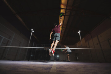two boys playing paddle tennis while one of them jumps to hit the ball.