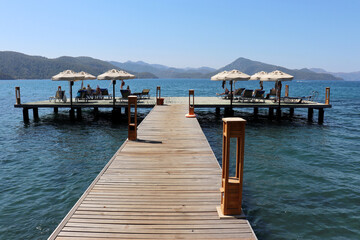 Beach holiday in resort on Mediterranean sea, people sunbathing on wooden pier with lounge chairs...
