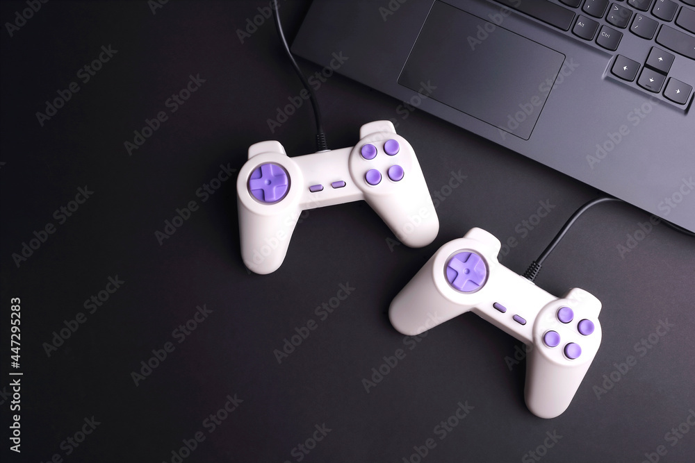 Poster two joystick game controllers with laptop on black background. top view. copy space.