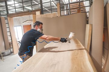 Man in respirator mask painting wooden planks at workshop. Craftsman modern furniture factory paint