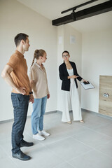 Full length portrait of female real estate agent giving apartment tour to young couple buying new...