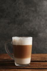 Glass cup of delicious layered coffee on wooden table against grey background, space for text