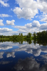 A warm summer day on the lake. Clouds in the blue sky. Lush forest and almost calm lake.