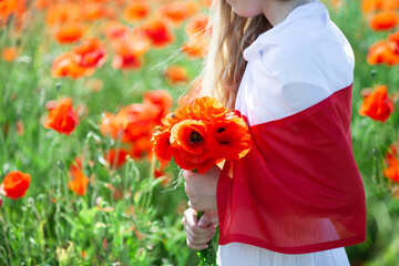 Close up of girl covered with flag of Poland holding bouquet of poppies in the poppy field. Polish Flag Day. Independence Day. Love Poland concept.