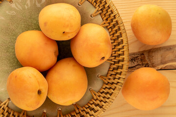 Several organic ripe apricots on a ceramic dish, on a wooden table, close-up, top view.