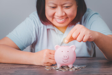 Obraz na płótnie Canvas Happy smiling, woman hand putting money coin into pink piggy bank saving money for future plan and retirement fund, Female smile show putting coin saving and investment money for prepare financial.