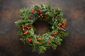 Christmas wreath of fresh natural spruce branch with red berries on brown background. New Year. Top...