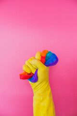 Hand in yellow rubber glove smashes rainbow anti stress pop it toy on pink background. Creative concept. Minimal abstract art