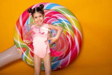 Cute arab little girl in swimming suit and swimming inflatable ring smiling having fun on yellow background.