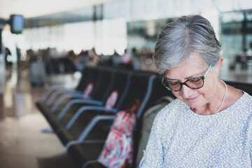 Portrait of mature woman sitting in airport with luggages using mobile phone waiting for departure of flight. Coronavirus and freedom concept