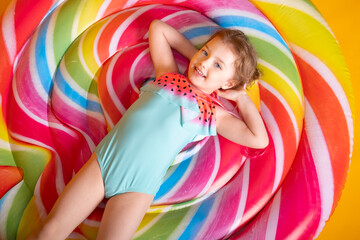 Funny little girl in swimming suit with swimming inflatable ring smiling having fun on yellow background.