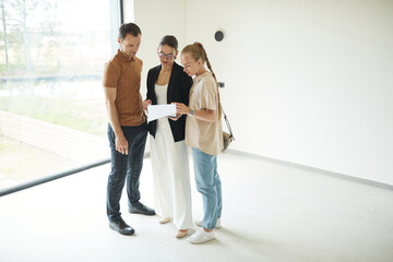 Minimal full length portrait of female real estate agent wearing mask while giving apartment tour to young couple, copy space