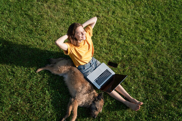 Beautiful happy young woman sitting on the grass with laptop and dog, top shot view