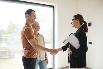 Side view portrait of young couple shaking hands with real estate agent during apartment tour, copy...