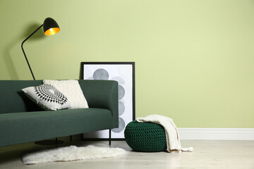 Stylish living room interior with comfortable knitted pouf and sofa near light green wall, space...