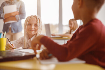 Happy pupil looking at her classmate at lesson