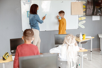 Teacher and schoolboy standing near the blackboard in the classroom