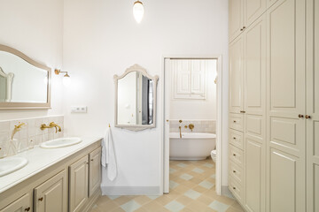 Interior of retro or classic style bathroom decorated in beige color with bath zone, big wardrobe, two sinks and vintage mirrors.