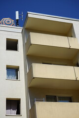 Wohnhaus mit Balkons in Beige und Sonnenschirm mit Mobilfunkmast auf dem Dach bei blauem Himmel und...