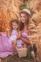 Close-up portrait of mother with daughter in straw hats in wheat field with dew drops. Young woman...