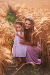 Close-up portrait of mother with daughter in straw hats in wheat field with dew drops. Young woman...
