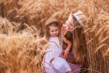 Close-up portrait of mother with daughter in straw hats in wheat field with dew drops. Young woman have fun with girl, tickle each other with golden ears of rye, laugh hug kiss each other. Countryside