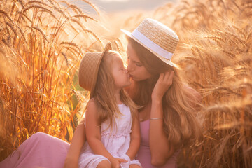 Close-up portrait of mother with daughter in straw hats in wheat field with dew drops. Young woman...
