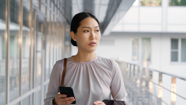 Asian businesswoman commuting to work checking messages on mobile phone outside office building