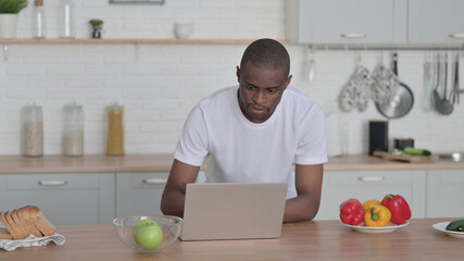 African Man Working on Laptop in Kitchen 