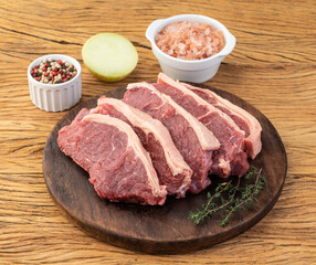 Sliced raw strip loin meat over wooden board with seasonings