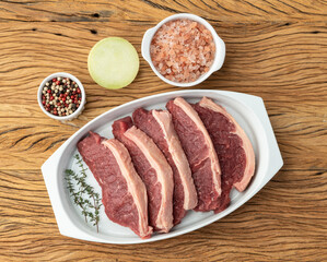 Sliced raw strip loin meat over white plate with seasonings