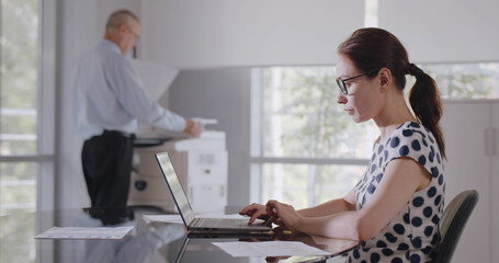 Obraz premium Side view of caucasian businesswoman sitting at desk in office using computer.