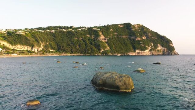Rocks over the sea at sunset along Ischia Citara Beach. Drone moving over the water - Italy