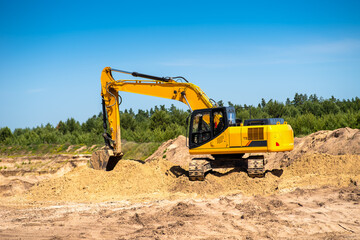 Obraz premium An industrial yellow excavator develops in a sandpit quarry. Industry, technology, mining. Heavy industrial machinery.