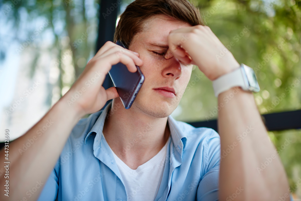 Poster emotional young man 20s unhappy with received bad news during phone call via smartphone device, upse