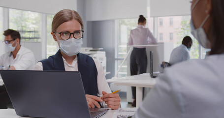 View over shoulder of african female client in safety mask at meeting with bank manager