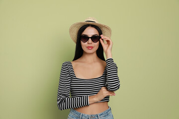 Fototapeta premium Beautiful young woman with straw hat and stylish sunglasses on light green background