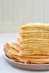 Traditional Russian Crepes Blini stacked in a white plate on light background. Maslenitsa...