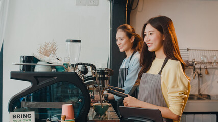 Beautiful young Asia lady barista working with coffee machine in coffee shop. Two small business...