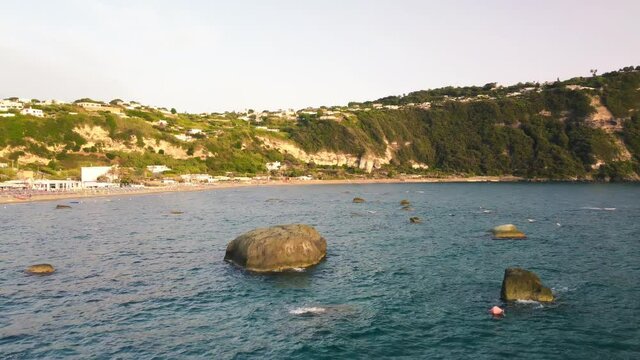 Rocks over the sea at sunset along Ischia Citara Beach. Drone moving over the water - Italy
