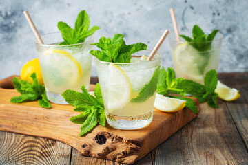 Two glass with lemonade or mojito cocktail with lemon and mint, cold refreshing drink or beverage with ice on rustic blue background