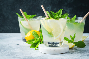 Two glass with lemonade or mojito cocktail with lemon and mint, cold refreshing drink or beverage with ice on rustic blue background