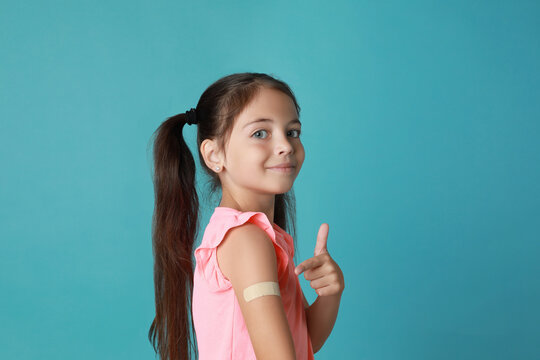 Vaccinated little girl showing medical plaster on her arm against light blue background