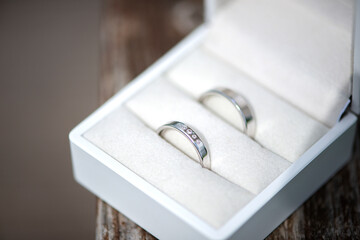 Close-up of two wedding silver rings in a beautiful white box on wooden background.