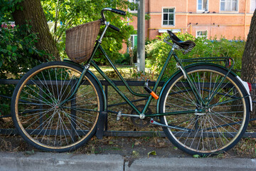 Fototapeta na wymiar stylish green vintage retro bike with wicker basket parked in the city